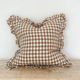 Brown and white checkered pillow with ruffled edges on a wooden surface.