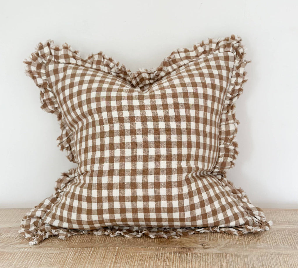 Brown and white checkered pillow with ruffled edges on a wooden surface.