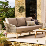 Outdoor patio with beige sofa, coffee table, and decorative items against a stone wall.