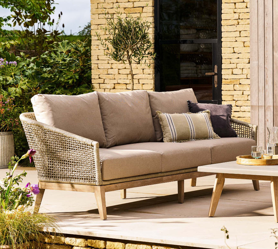 Outdoor patio with beige sofa, coffee table, and decorative items against a stone wall.