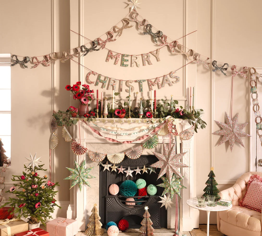 Decorated living room with Christmas decorations, including a 'Merry Christmas' banner and festive items around a fireplace.