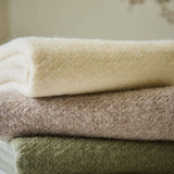 Stack of folded wool blankets  in beige, brown, and green on a neutral background