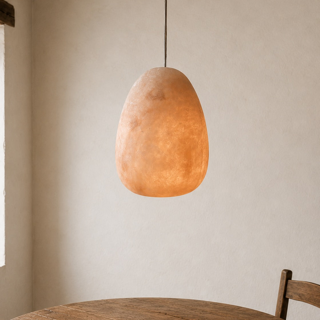Round wooden table with a pendant light fixture against a neutral wall.