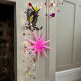 Decorative pink star hanging on a door with colorful lights and ornaments.