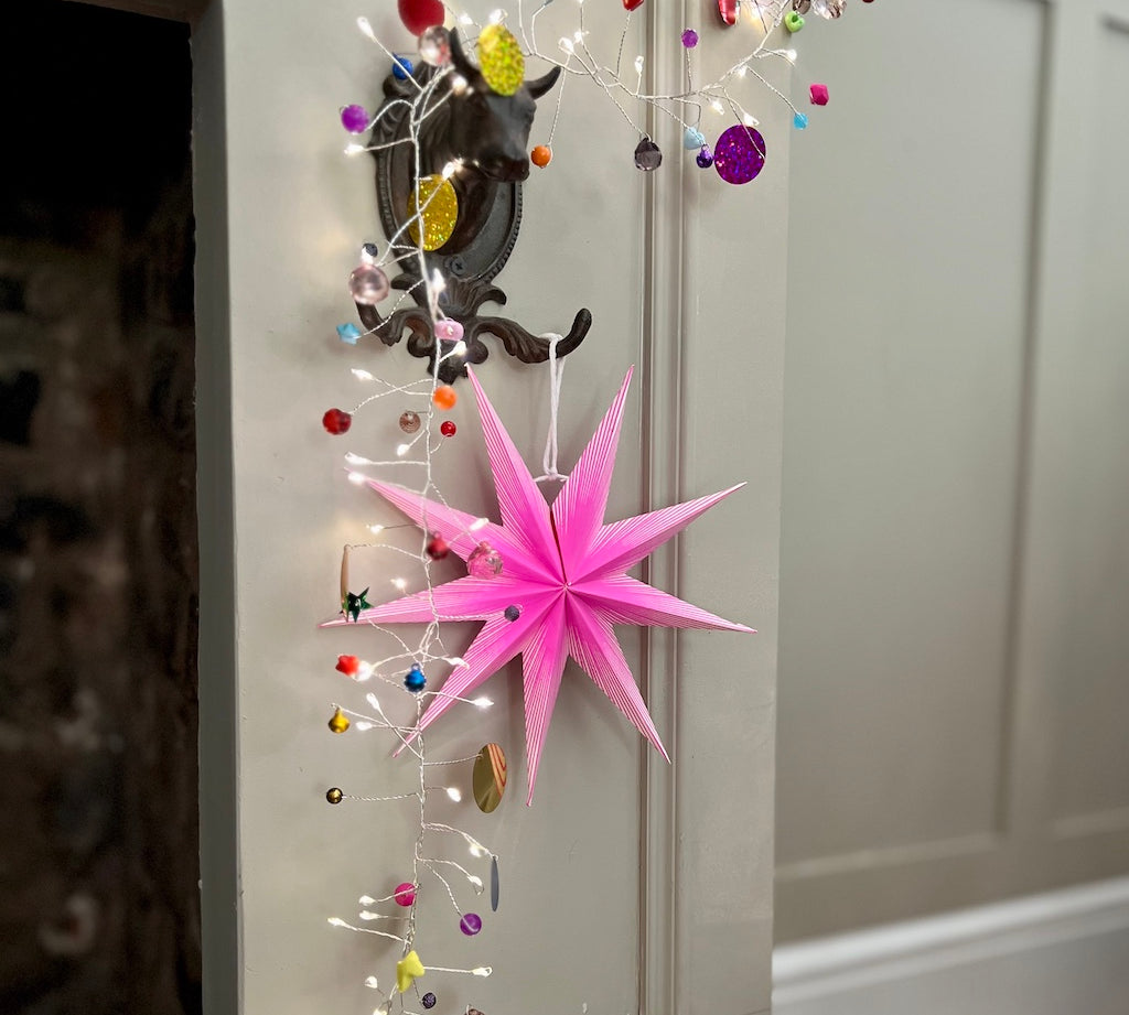 Decorative pink star hanging on a door with colorful lights and ornaments.