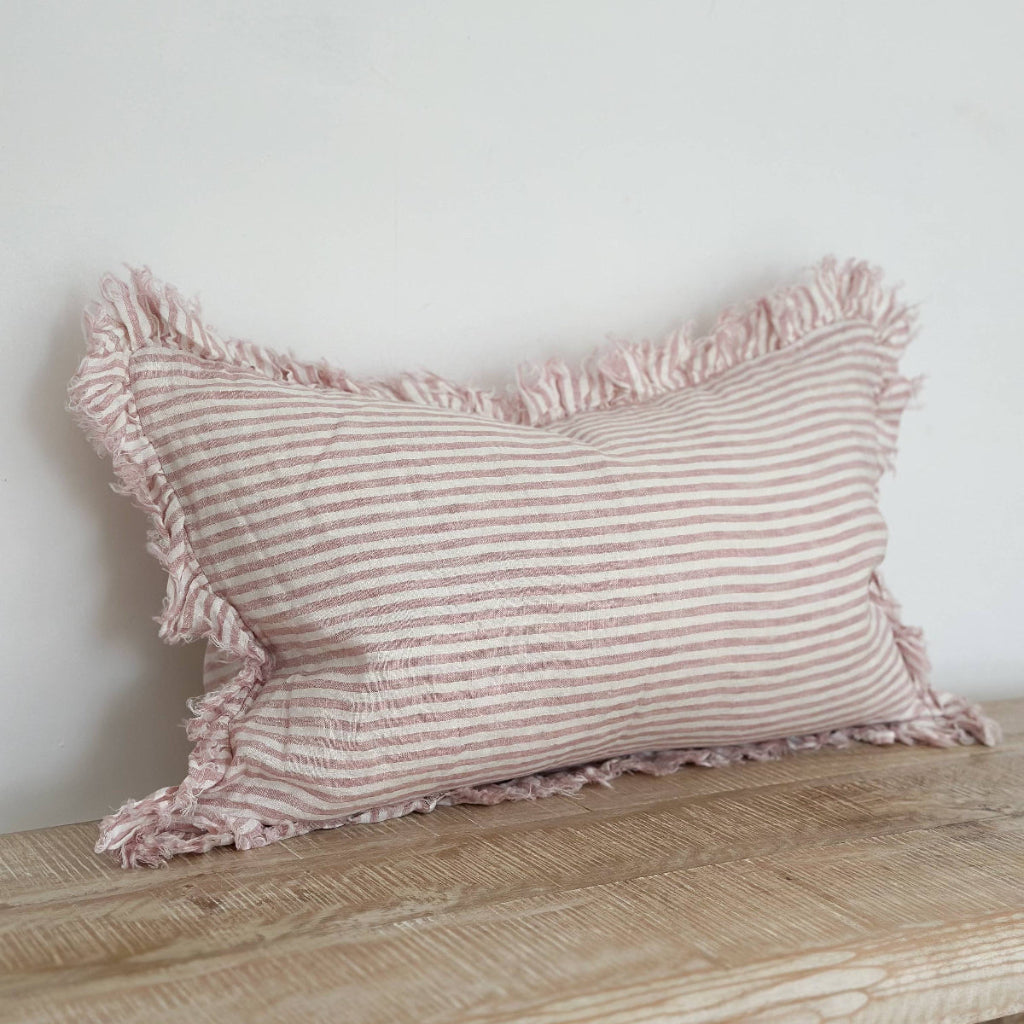 Striped pillow with ruffled edges on a wooden surface against a white wall