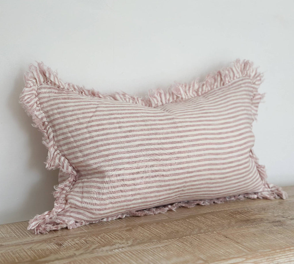 Striped pillow with ruffled edges on a wooden surface against a white wall