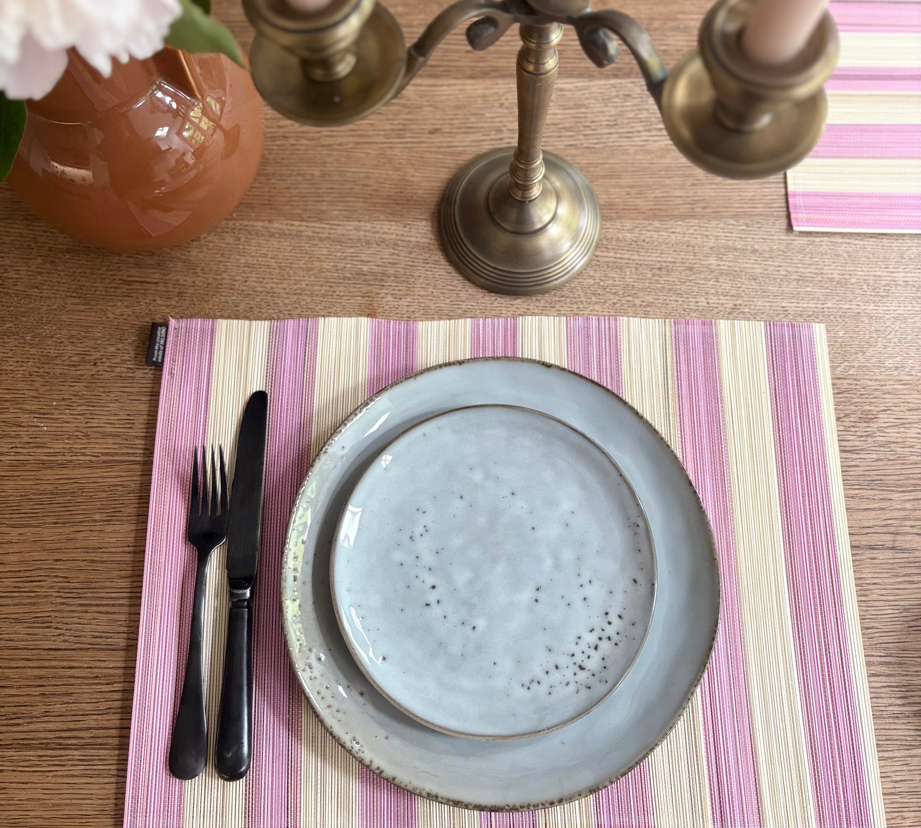 Table setting with a blue plate, cutlery, and striped placemat on a wooden table.