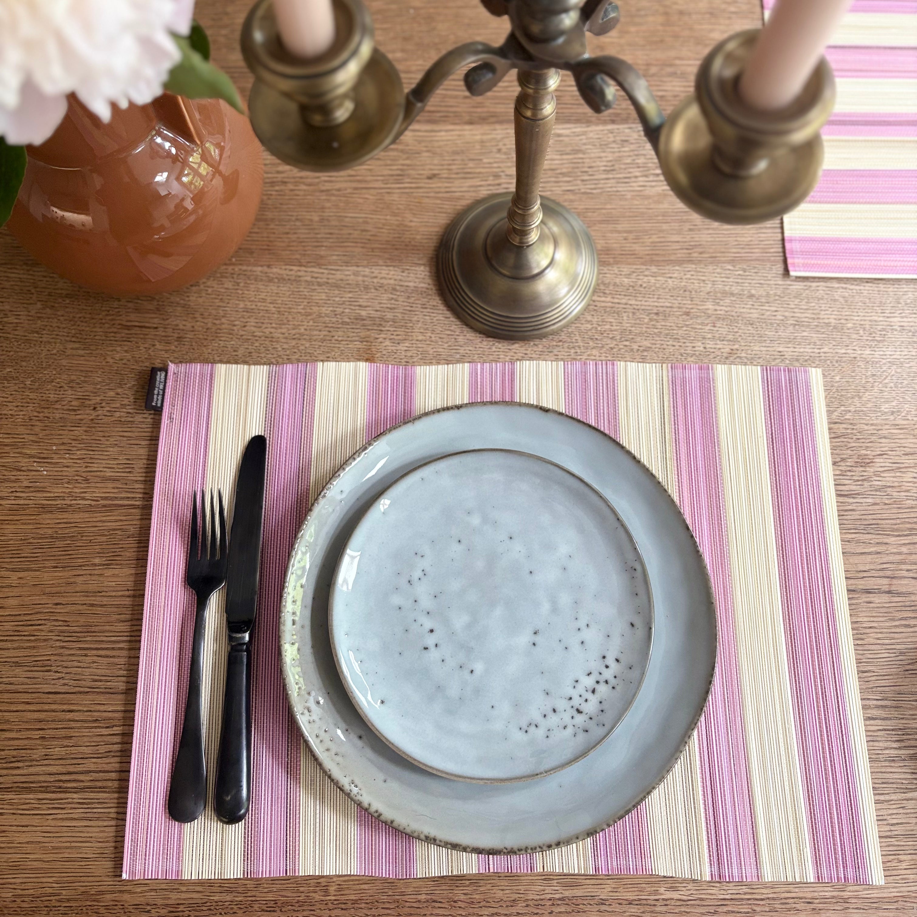 Table setting with a blue plate, cutlery, and striped placemat on a wooden table.