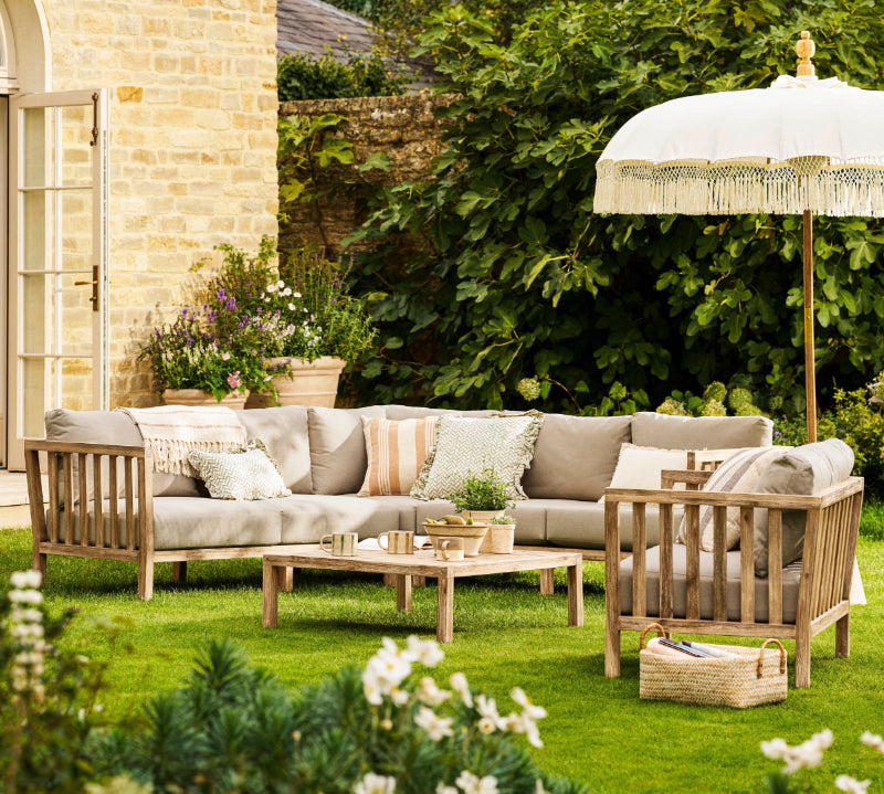 Outdoor Porthallow corner sofa with wooden furniture, umbrella, and plants in a garden setting.