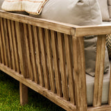 Wooden outdoor sofa with beige cushions on a grassy area