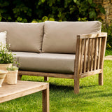 Outdoor wooden Porthallow sofa with beige cushions on a grassy area