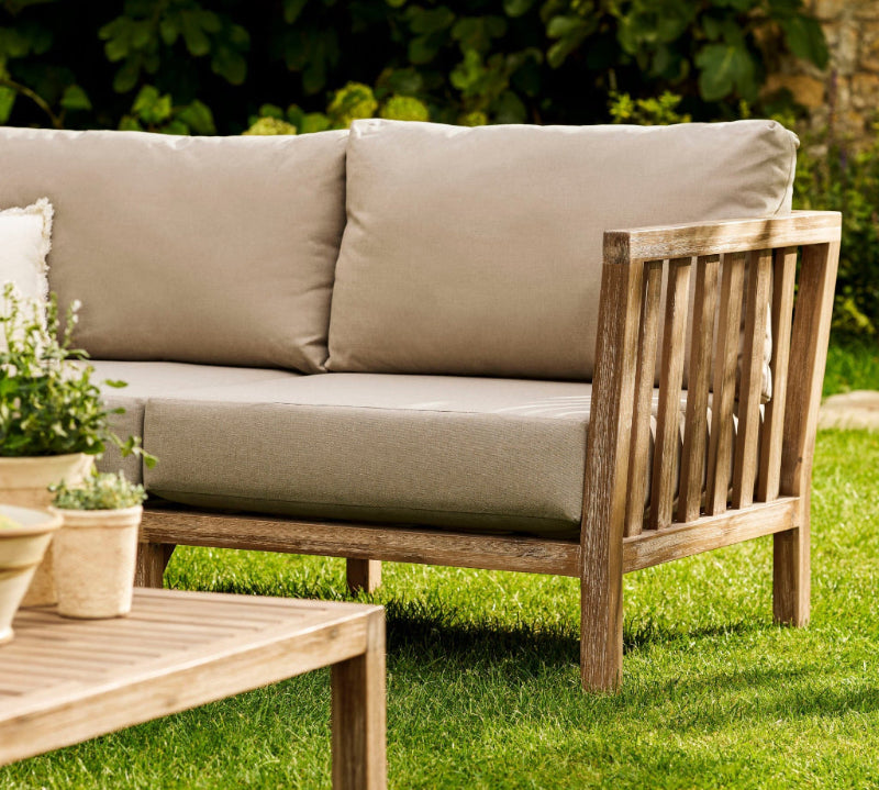 Outdoor wooden Porthallow sofa with beige cushions on a grassy area