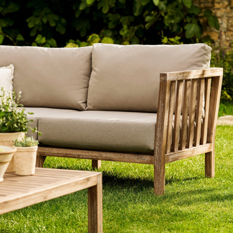 Outdoor wooden Porthallow sofa with beige cushions on a grassy area