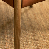 Close-up of a wooden chair leg with a natural wood grain finish resting on a woven jute rug.
