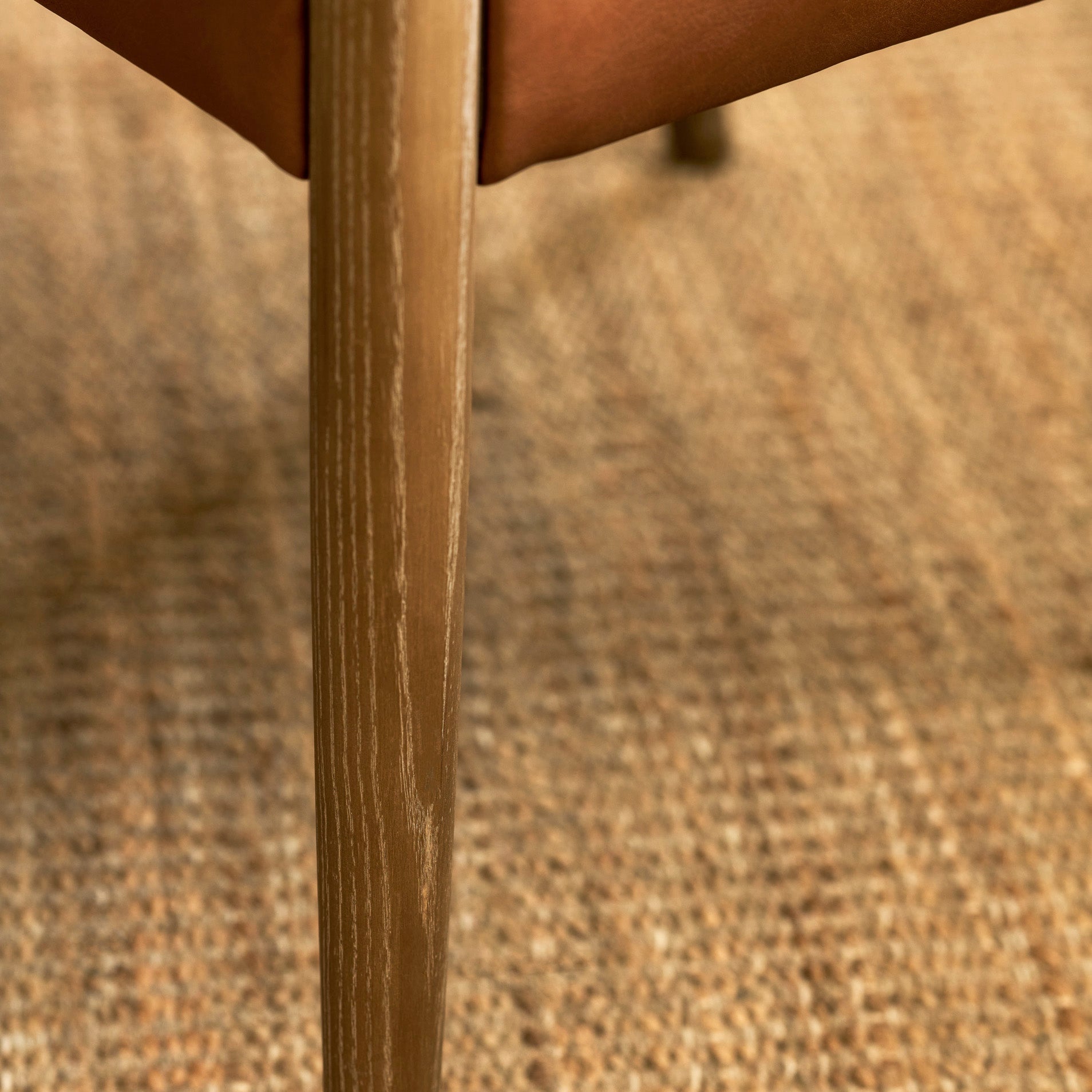 Close-up of a wooden chair leg with a natural wood grain finish resting on a woven jute rug.