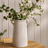 White textured vase with greenery on a wooden surface against a light gray wall.
