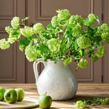 White pitcher with green flowers on a wooden table with apples