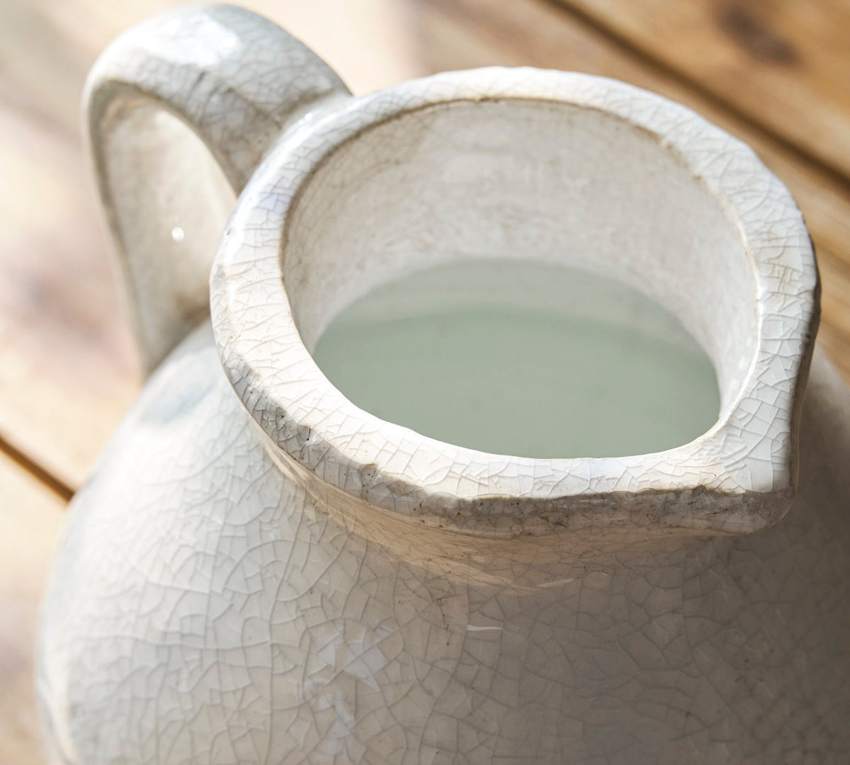 Ceramic white jug with a handle filled with water on a wooden surface