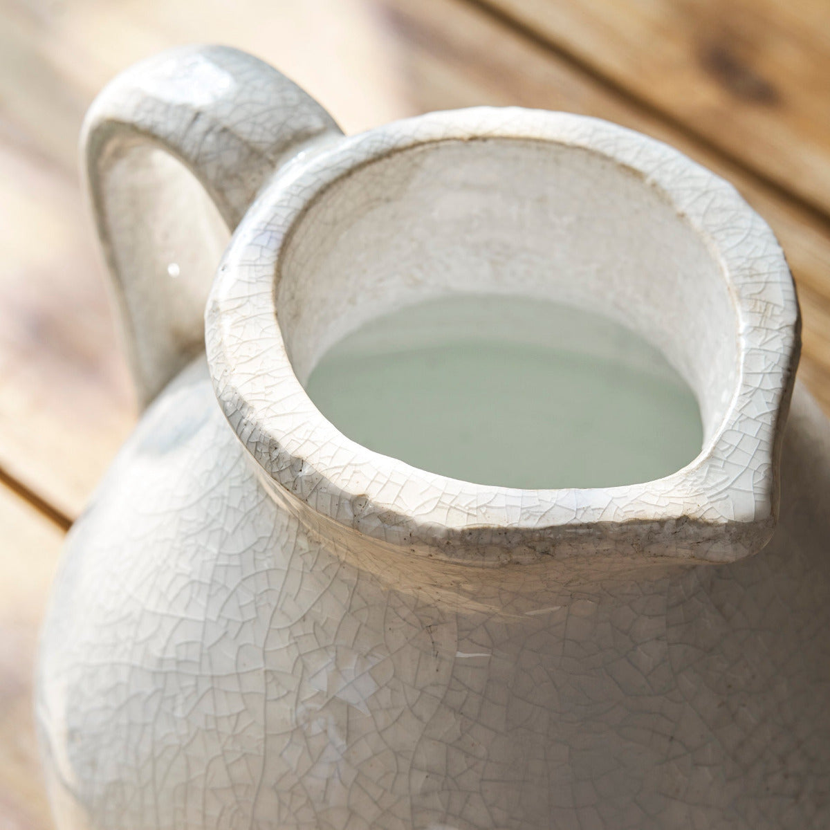 Ceramic white jug with a handle filled with water on a wooden surface