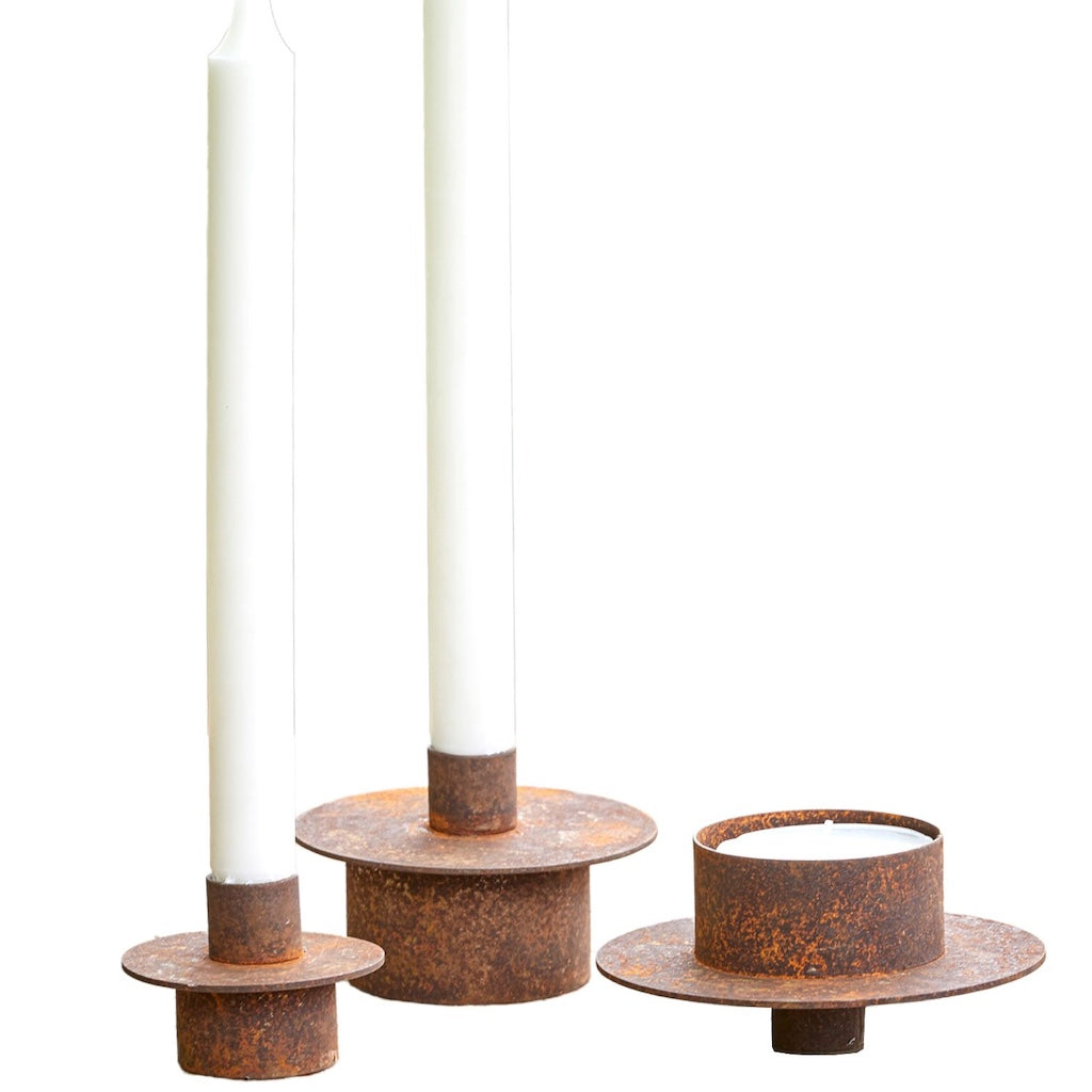 Set of three rusted metal candle holders with white candles on a white background