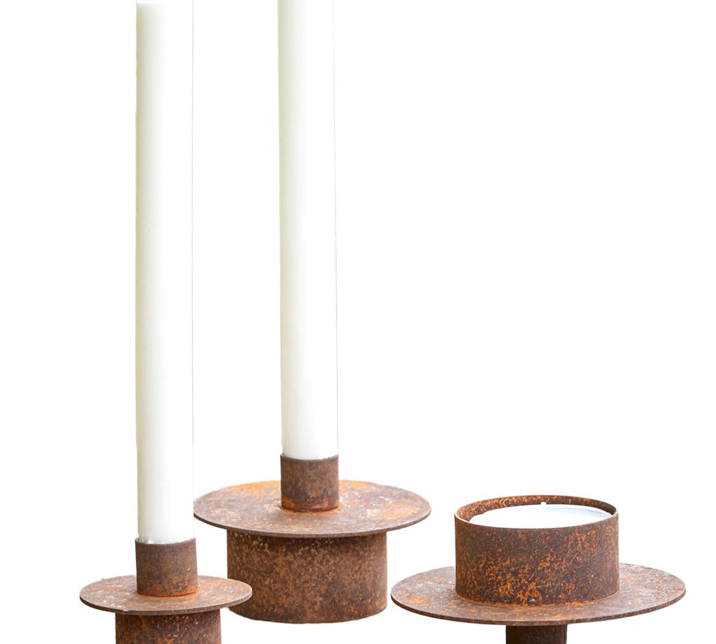 Set of three rusted metal candle holders with white candles on a white background
