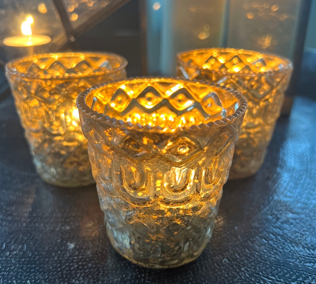 Three textured glass candle holders with lit candles on a dark surface