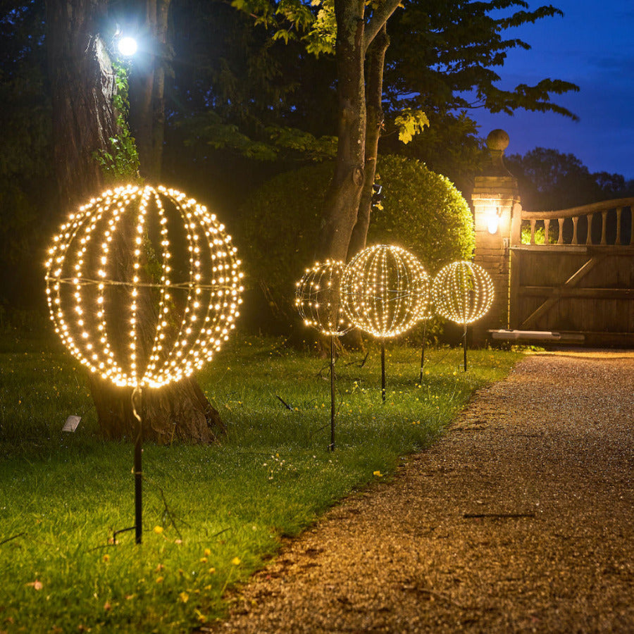 Decorative outdoor lights shaped like spheres on a grassy area at night.