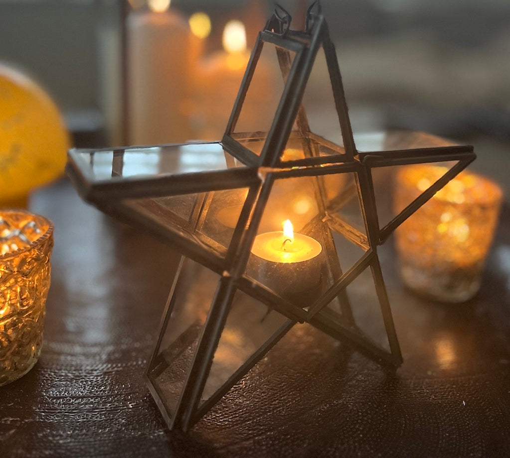 Star-shaped glass lantern with a candle inside on a wooden surface.