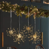 Three hanging starburst LED light decorations with warm white lights, displayed in a dining room setting below a decorated garland.