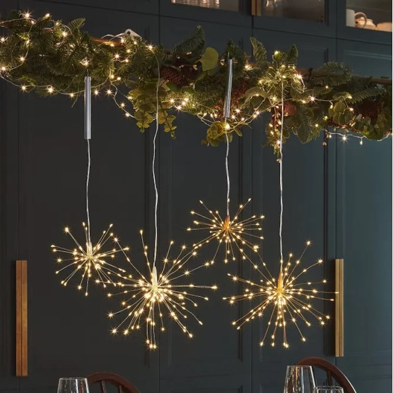 Three hanging starburst LED light decorations with warm white lights, displayed in a dining room setting below a decorated garland.