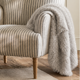 A classic armchair with beige and gray vertical stripes, styled with a fluffy light gray throw blanket draped over one arm, set in a warm, neutral-toned living room.