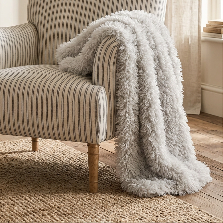 A classic armchair with beige and gray vertical stripes, styled with a fluffy light gray throw blanket draped over one arm, set in a warm, neutral-toned living room.