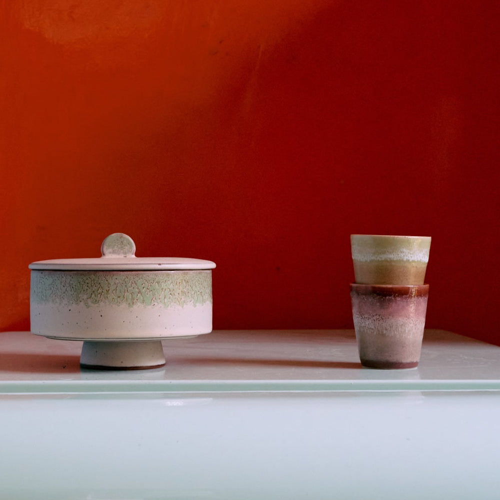 Two ceramic containers on a reflective surface with an orange wall background