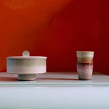 Two ceramic containers on a reflective surface with an orange wall background