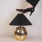 Gold disco ball table lamp with black pleated shade and high-heeled foot stepping on it.