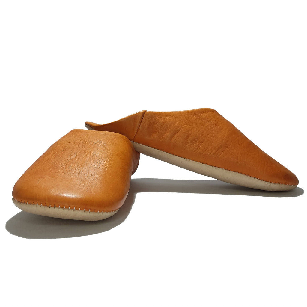 A pair of tan leather slip-on shoes with a contrasting off-white sole, displayed on a clean white background.