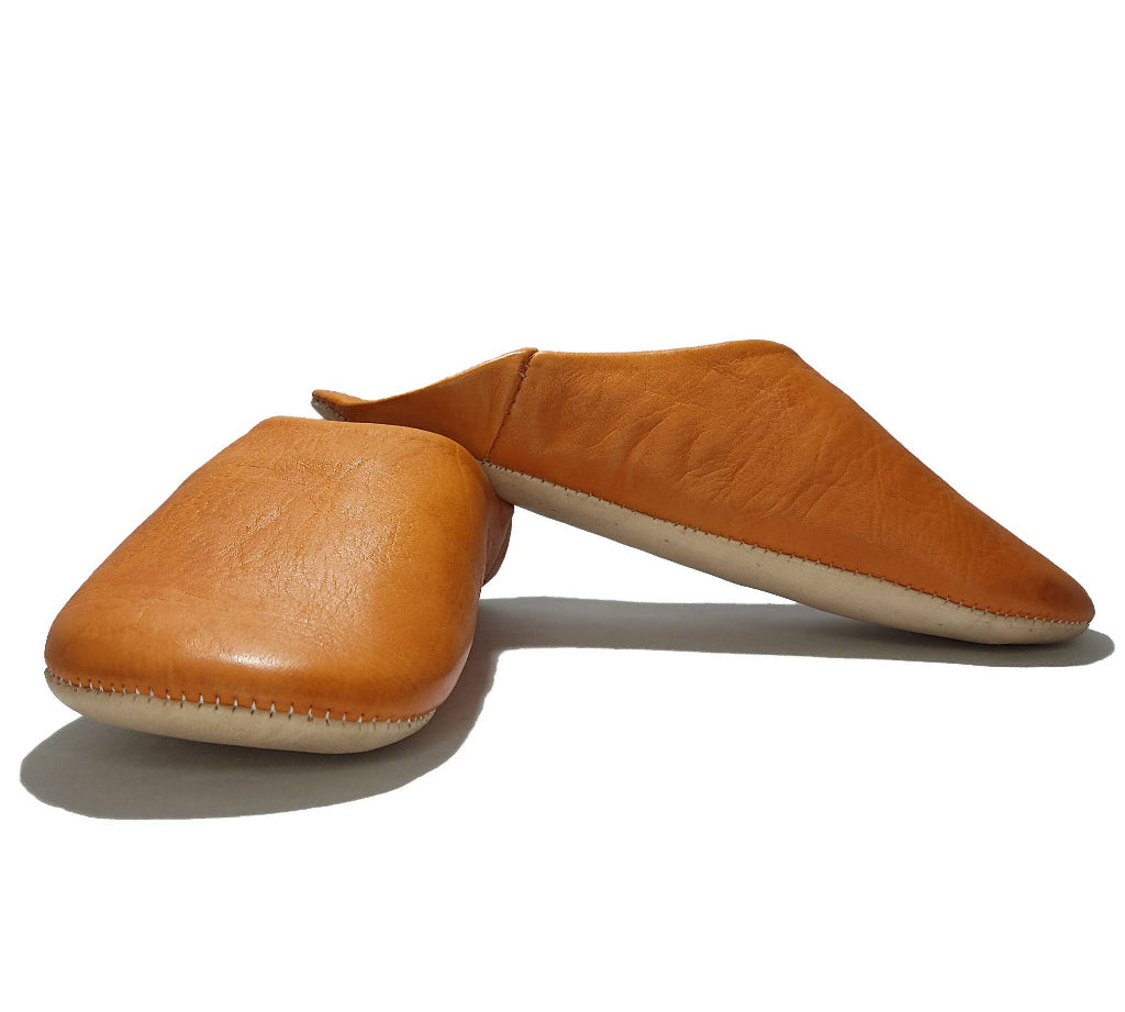 A pair of tan leather slip-on shoes with a contrasting off-white sole, displayed on a clean white background.