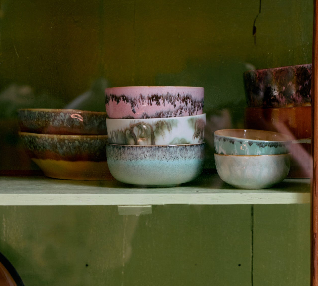 Collection of ceramic bowls on a shelf with a wooden frame and green wall background