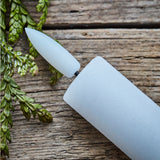 White LED candle with a pointed top on a wooden surface with green leaves.