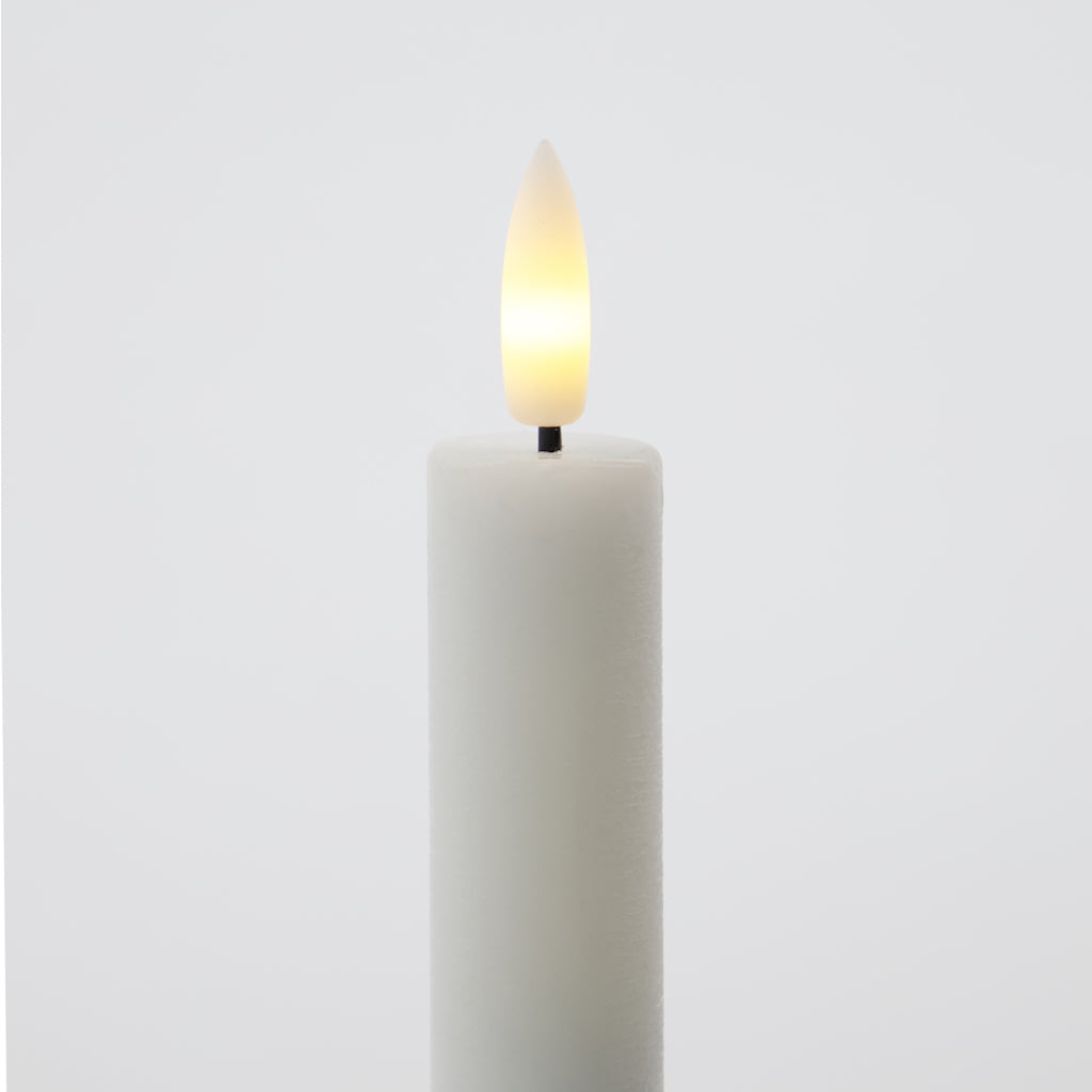 White candle with a lit LED wick on a light gray background