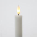 White candle with a lit LED wick on a light gray background