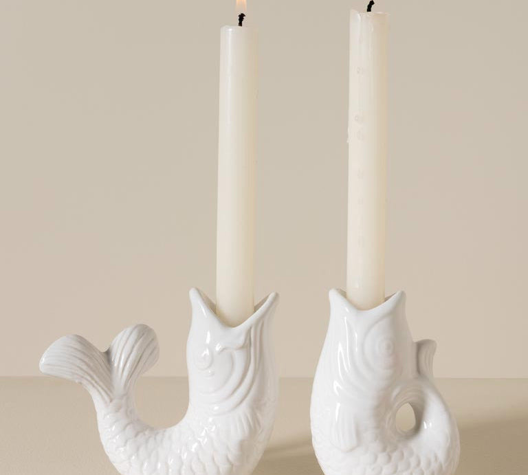 Two white ceramic candle holders shaped like fish with lit candles inside on a beige background.