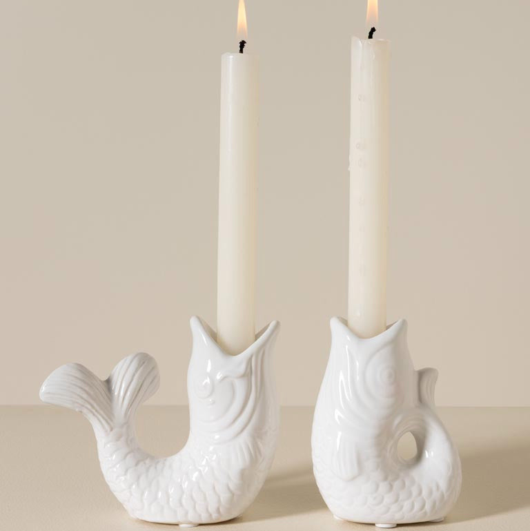 Two white ceramic candle holders shaped like fish with lit candles inside on a beige background.
