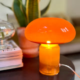 Orange mushroom-shaped lamp on a table with a plant and books in the background