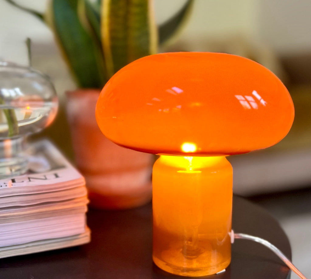 Orange mushroom-shaped lamp on a table with a plant and books in the background