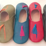 Four pairs of colorful babouche slippers with tassels on a white background