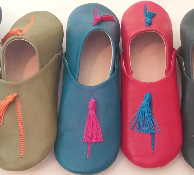 Four pairs of colorful babouche slippers with tassels on a white background