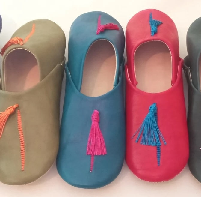 Four pairs of colorful babouche slippers with tassels on a white background