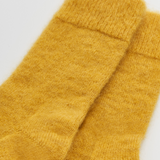 A close-up of a pair of soft, fuzzy mustard yellow knit socks on a plain white background.